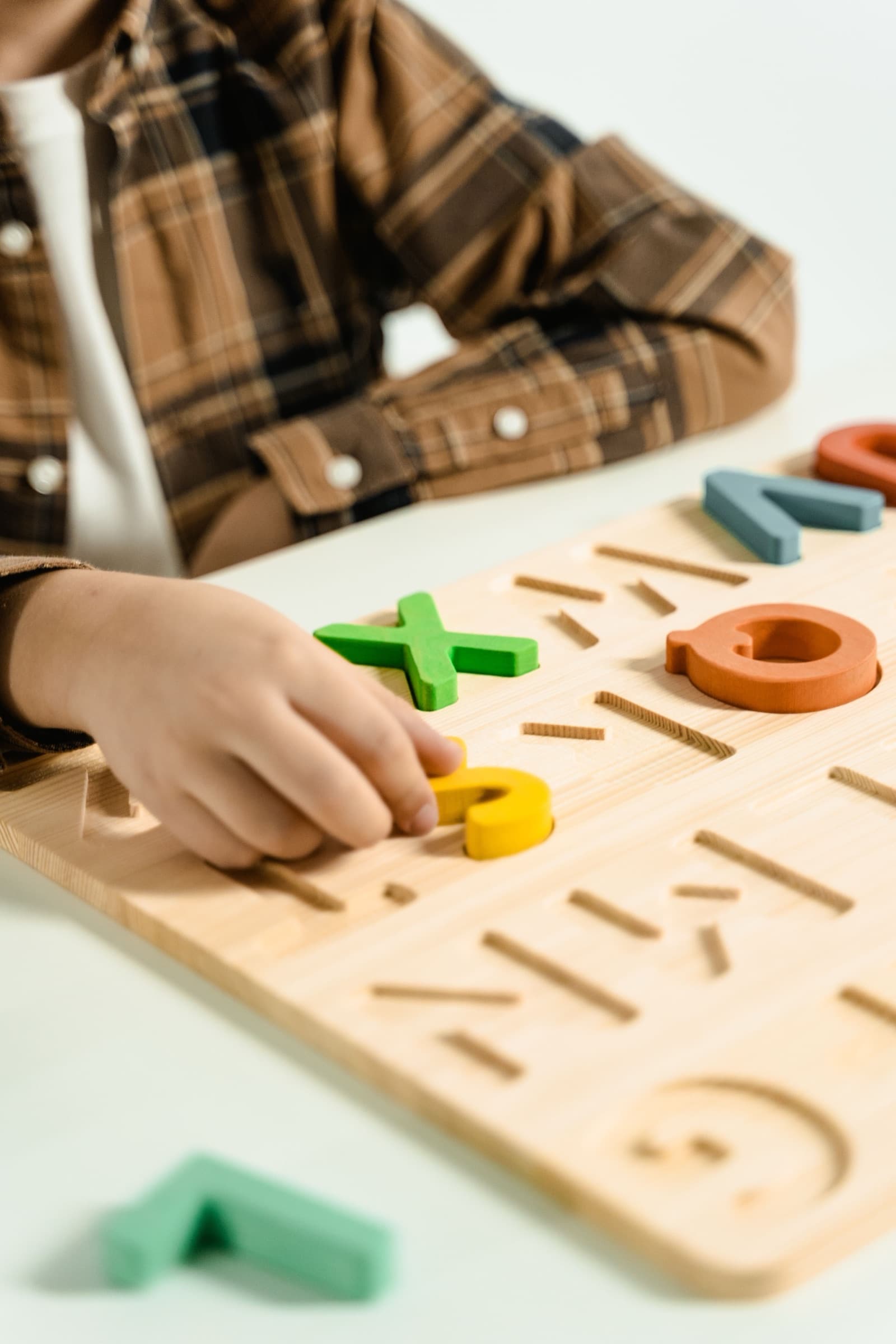 Kinderhand legt Holzbuchstaben in ein Steckbrett