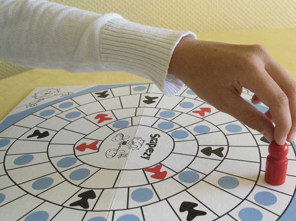 Hand setzt eine Spielfigur auf ein Lernspielbrett